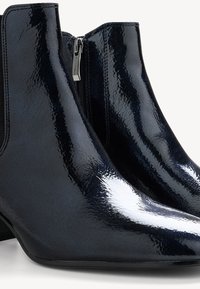 Bottines en cuir verni noir brillant avec fermeture éclair latérale et petits talons blocs, vue rapprochée montrant la texture et la brillance.