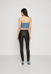 Kék mintás, pánt nélküli crop top, fekete, slim-fit nadrág és világoskék magassarkú cipő, hátulról, sima háttér előtt.