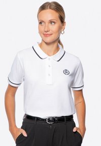 Camisa polo blanca con cuello y ribete de mangas negros, tapeta con tres botones y logo bordado en el lado izquierdo del pecho. Textura de algodón suave.