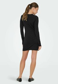 Svart klänning med långa ärmar och subtilt stjärnmönster, figursydd design och mjukt tyg. Kombinerad med platta skor med dekorativa detaljer.