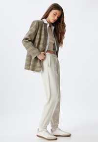 Geruite blazer in beige met dunne strepen, korte beige top, lichtgrijze sweatpants en witte sneakers met gumleesten. Casual outfit.