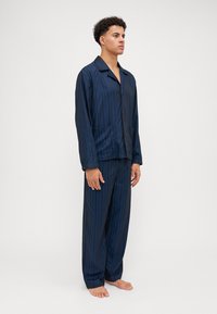 Navy blue striped pajama set, made of smooth fabric, features a button-up top with a collar and two front pockets; loose-fitting pants.