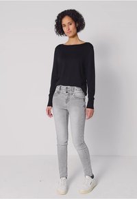 Musta pitkähihaine villapaita yhdistettynä vaaleanharmaisiin slim fit -farkkuihin. Valkoiset lenkkarit viimeistelevät asun. Kankaan sileys ja slim fit -malli huomioitu.