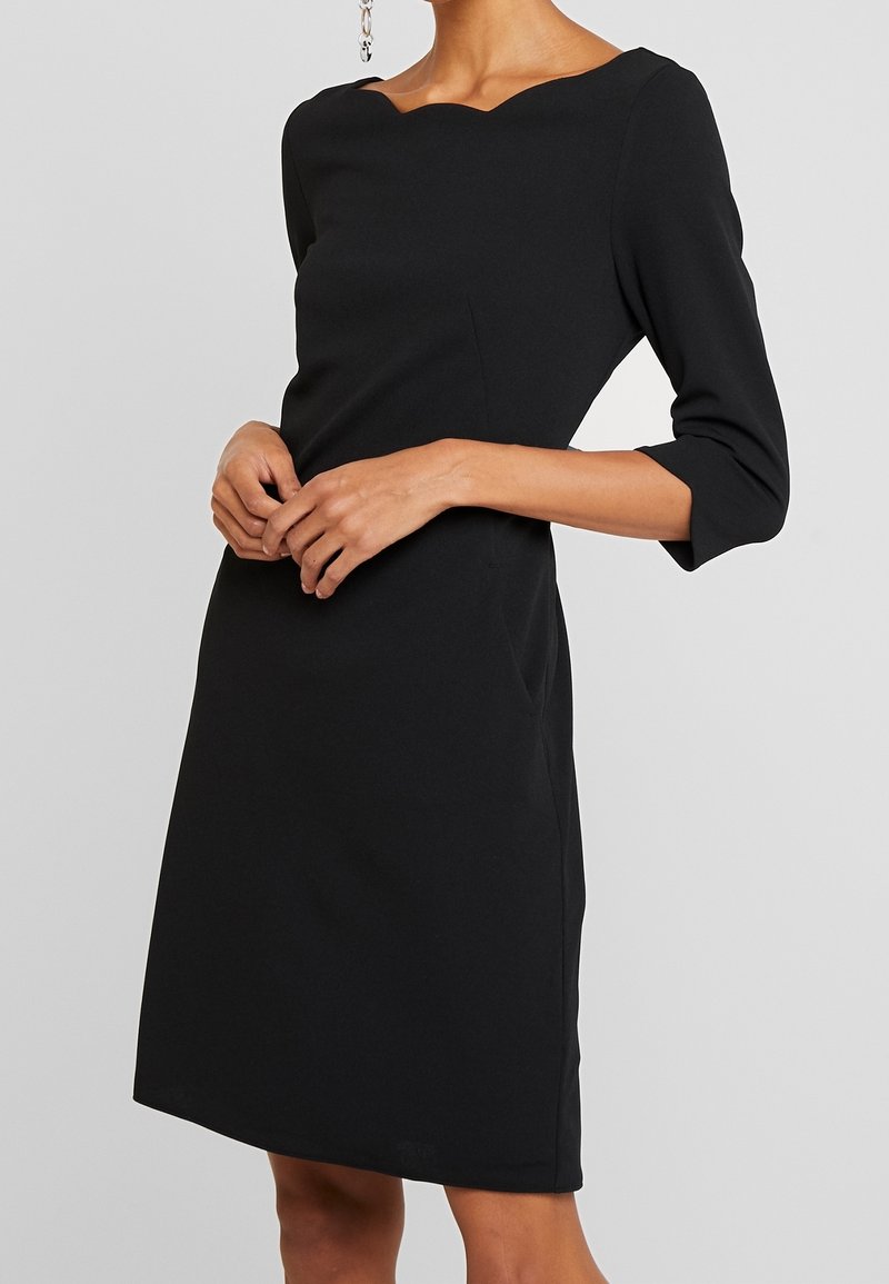 Černé, přiléhavé šaty s vykrojeným výstřihem a tříčtvrtečními rukávy. Vyrobené z hladkého materiálu, s jemnými bočními švy a délkou ke kolenům.