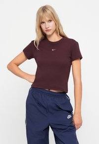 Bordo trumpas marškinėliai su trumpomis rankovėmis ir apvaliu iškirpimu. Papuošti mažu baltu Nike logotipo ženklu ant krūtinės. Derinami su tamsiai mėlynomis kelnėmis.