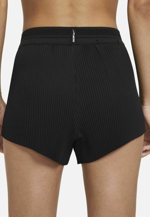 Bagudvendt billede af person iført sorte plisserede sportsshorts med bred taljebånd og "RACING" mærkat i midten.