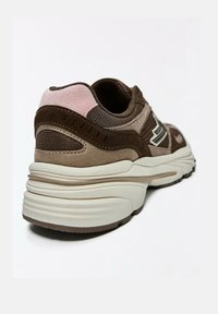 Chaussure de sport marron et beige avec un accent en suède rose au talon et une semelle blanche épaisse, vue en angle arrière sur fond blanc.