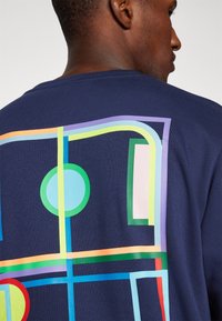 Marineblaues T-Shirt mit einem bunten, abstrakten geometrischen Design auf dem Rücken, bestehend aus Kreisen und Linien in verschiedenen Pastellfarben. Aus Baumwolle, kurze Ärmel.