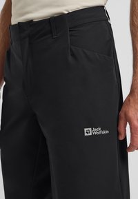 Schwarze Outdoor-Hosen aus glattem Stoff, mit einer Seitentasche und einem sichtbaren Jack Wolfskin-Logo in Weiß. Entwickelt für Komfort und Funktionalität.