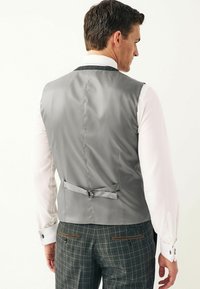 Grå vest med en glat tekstur, tætsiddende design og justerbar rem med spænde på bagsiden, parret medternet bukser.