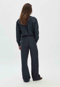 Tummansininen pitkähihainen paita, jossa on rento istuvuus, yhdistettynä samanvärisiin leveälahkeisiin housuihin, joissa on joustava vyötärö ja kaksi takataskua.