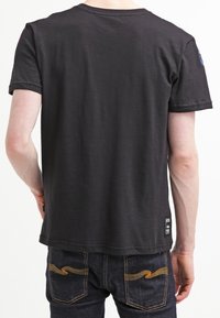 Svart kortärmad t-shirt med rund halsringning, tillverkad av mjukt tyg. Har en liten logotagg vid fållen och en avslappnad passform.