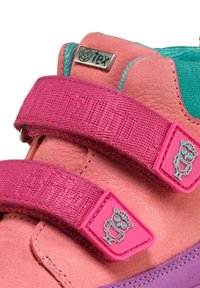 Gros plan sur une chaussure d'enfant rose et violette avec deux brides en Velcro roses, chacune ornée d'une icône de hibou bleu et d'une étiquette métallique portant l'inscription "tex".