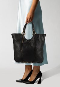 Borsa a tracolla nera in pelle con hardware dorato e dettagli borchiati, dotata di manici doppi. La borsa ha una finitura morbida e testurizzata e una parte superiore curva.