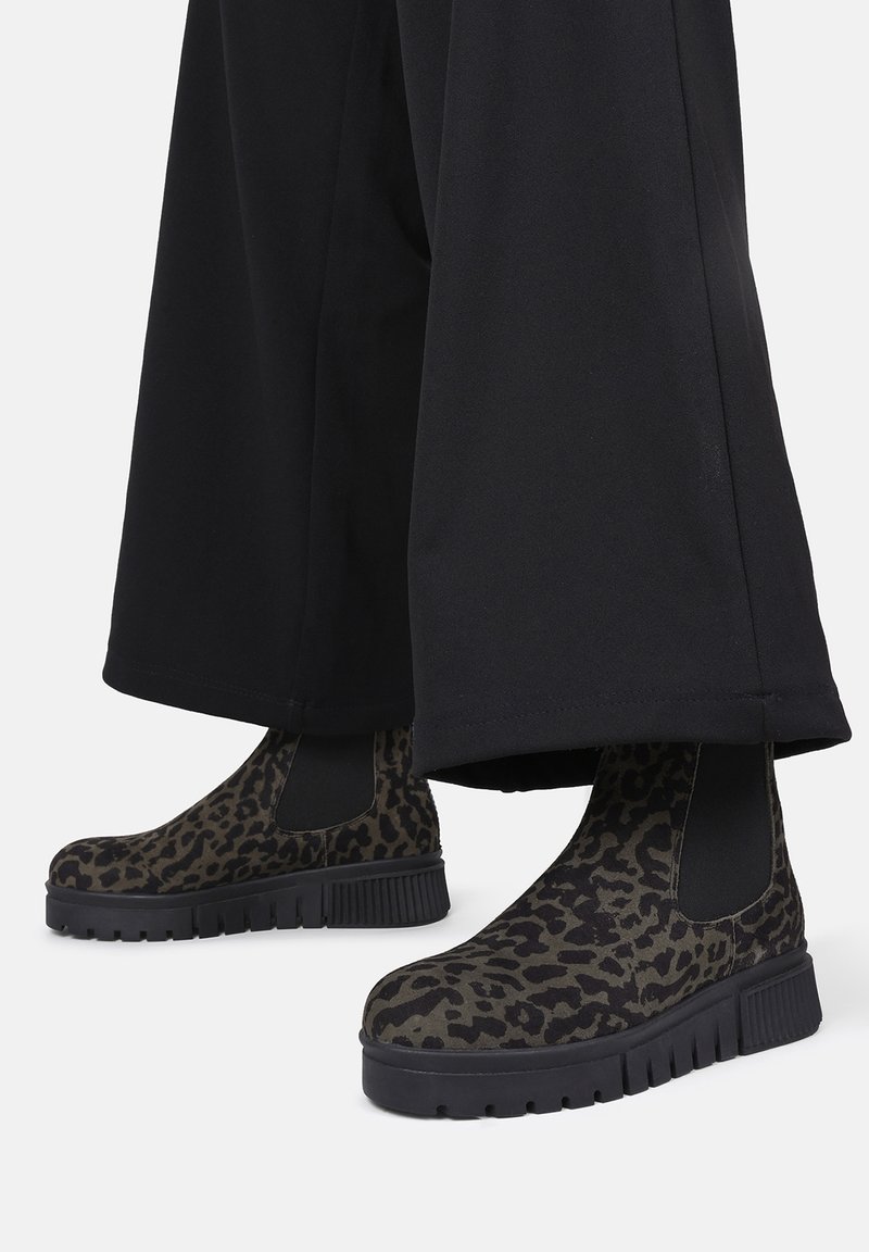 Stivali alla caviglia con stampa leopardata, pannelli laterali elastici neri, suole in gomma e un design con piattaforma spessa, abbinati a pantaloni neri a gamba larga.
