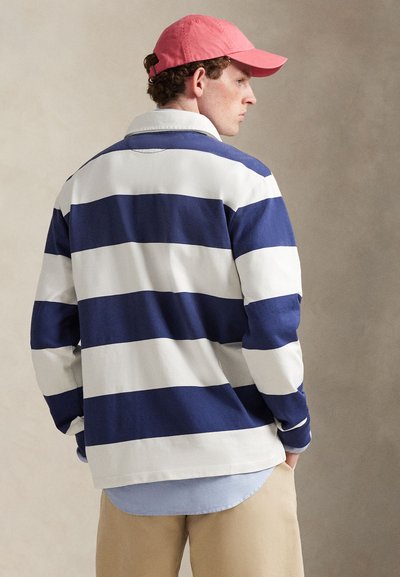 Maillot de rugby rayé en coton bleu marine et blanc, doté d'un col classique, de manches longues, et superposé avec une chemise bleu clair en dessous.