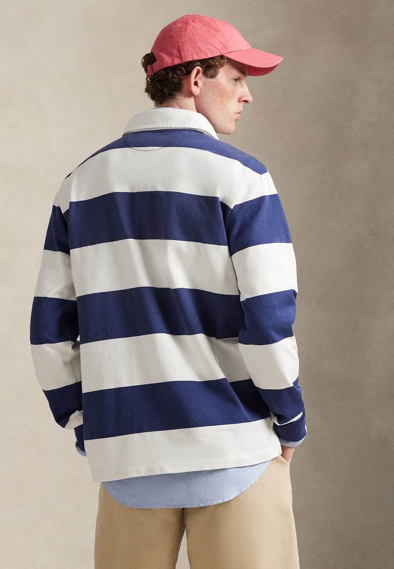 Striped rugby shirt in navy and white cotton, featuring a classic collar, long sleeves, and layered with a light blue shirt underneath.