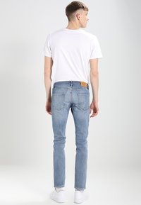 Helle blaue Skinny-Jeans mit einem taillierten Schnitt, ausgewaschenem Finish und einem braunen Lederpatch am Bund. Kombiniert mit einem schlichten weißen T-Shirt.