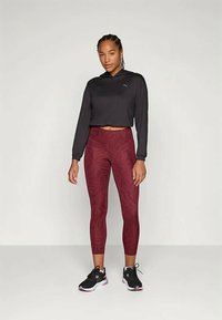 Black cropped hooded sweatshirt, dark red textured leggings, and black athletic shoes. Leggings feature a subtle pattern and fitted style.
