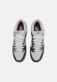 Nike sneakers with a white leather upper and grey textured accents, perforated toe, white laces, and a pink logo on the tongue.