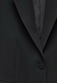 Blazer noir avec un seul bouton recouvert, un revers cranté et une texture de tissu lisse.