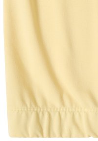 Gros plan sur un tissu jaune pâle avec un ourlet froncé et un détail de couture visible.