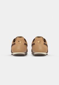 Καφέ σουέτ αθλητικά παπούτσια με καφέ λε�πτομέρειες, διακοσμημένα με χρυσό λογότυπο, στρογγυλή φτέρνα και λευκή σόλα, που επιδεικνύουν μια απαλή υφή και αθλητικό σχέδιο.