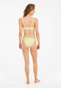 Žuti bikinijski set sa prugama, sa bandeau stilom i donjim dijelom na vezanje s bočne strane. Tkanina je glatka s suptilnim sjajem i elastičnim trakama.