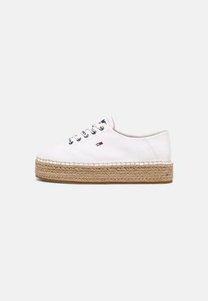 Hvid lærreds-sneaker med tyk flettet juteplatformsål og lille rød, hvid og blå logo på siden samt på øjenskyltens snørelapper.