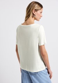 T-shirt en coton léger, à manches courtes, de couleur verte claire, avec un col rond et une coupe décontractée, présentant une texture lisse et un design simple.