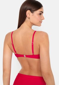 Bright pink bikini top with adjustable straps and a clasp closure at the back, featuring smooth, stretchy fabric.