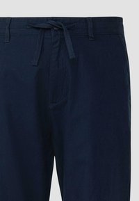 Pantalon bleu marine avec fermeture par bouton et zip, passants pour ceinture et cordon en tissu noué à la taille.