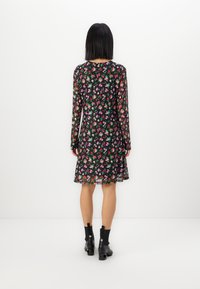 Robe fleurie à manches longues, base noire, ornée de fleurs rouges, roses et vertes. Longueur genou, tissu transparent. Portée avec des bottines noires.