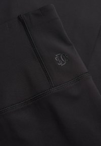 Czarne legginsy sportowe z gładką fakturą, płaskimi szwami i małym logo w kontrastowym kolorze.