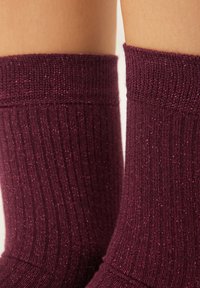 Bordeauxrote Socken mit einer gerippten Textur und metallischen Glitzereffekten. Die Bündchen sind elastisch und sorgen für einen engen Sitz am Knöchel.