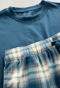 Blaues Baumwoll-T-Shirt, kombiniert mit karierten Shorts in den Farbtönen Blau, Grau und Gelb; elastischer Bund mit Kordelzug.