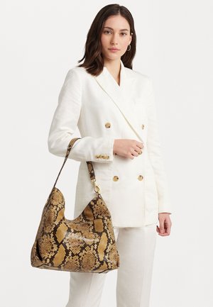 Donna con completo bianco tiene una grande borsa a tracolla in pelle con stampa serpente marrone chiaro e scuro, con dettagli in oro.
