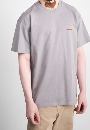 Gray cotton t-shirt with short sleeves, relaxed fit, and a small yellow and red Carhartt logo on the left chest. Smooth texture.