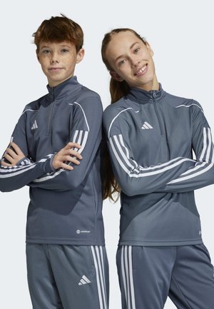 Due giovani che indossano giacche sportive grigie scure abbinate, con accenti e strisce bianche, dotate di colli alti e chiusure a zip.