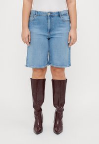 Denim kratke hlače v svetlo modri barvi s klasičnim pet-imenským dizajnom, v kombinaciji z burgundskimi sijajnimi škornji do kolen z ostrimi prsti.