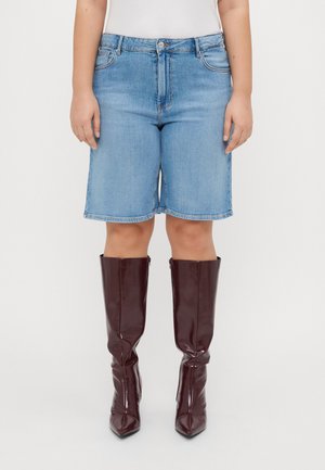 Shorts in denim chiaro con un design classico a cinque tasche, abbinati a stivali lucidi bordeaux al ginocchio con punta affusolata.