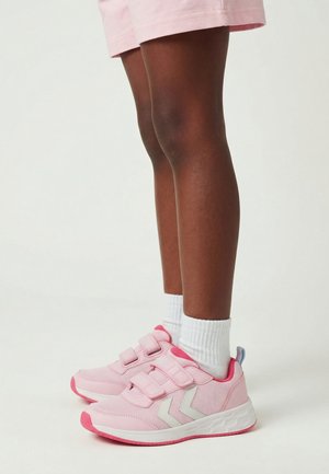 Barn iført lyserøde sneakers med velcro, hvide sokker og lyserøde shorts, stående på hvid baggrund.