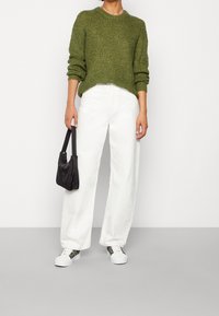 Grön stickad tröja, vita vida byxor, svart handväska och vita sneakers med färgglada mönster. Enkelt design, texturerad tyg.