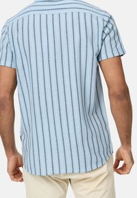 Camisa de manga corta en azul claro con rayas verticales oscuras, hecha de tela ligera. Cuenta con una pieza trasera y dobladillo curvado.