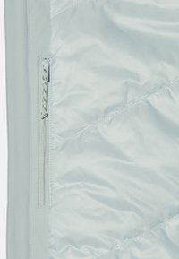 Veste matelassée bleu clair avec une texture lisse et brillante. Présente une fermeture éclair sur le côté et un motif de couture en diagonale pour plus de détails.