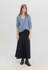 Suéter de canalé azul claro con escote en V, combinado con una falda larga de canalé negra y botas negras de tobillo. Diseño simple y texturizado.