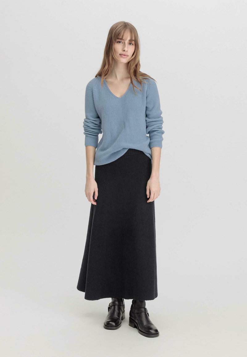 Suéter de canalé azul claro con escote en V, combinado con una falda larga de canalé negra y botas negras de tobillo. Diseño simple y texturizado.