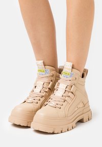 Baskets montantes beiges en matériau synthétique texturé, avec des semelles épaisses, un design à lacets et des tirettes de marque.