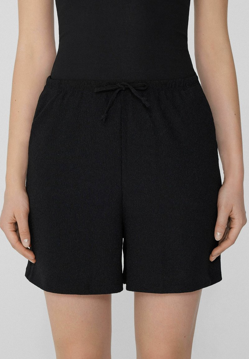 Pantaloni corti neri con vita elastica e coulisse, caratterizzati da un tessuto testurizzato e fessure laterali per maggiore comfort e stile.