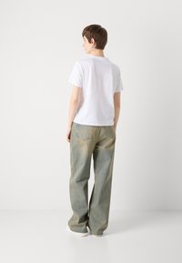 Tricou alb cu mânecă scurtă, asortat cu pantaloni din denim bleu deschis, cu croială largă. Țesătură texturată cu cusături standard și buzunare pe spate.